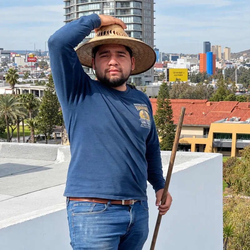 Trabajador con sombrero de paja y camisa azul en una azotea con la ciudad al fondo