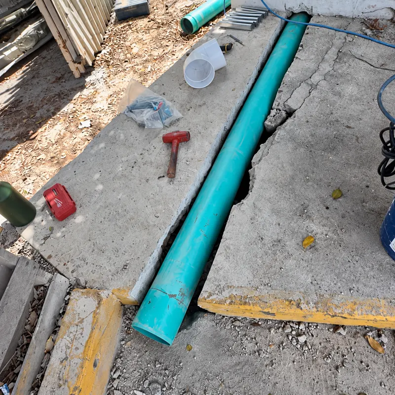 Tubería turquesa en una zanja abierta en el concreto, rodeada de conexiones y herramientas