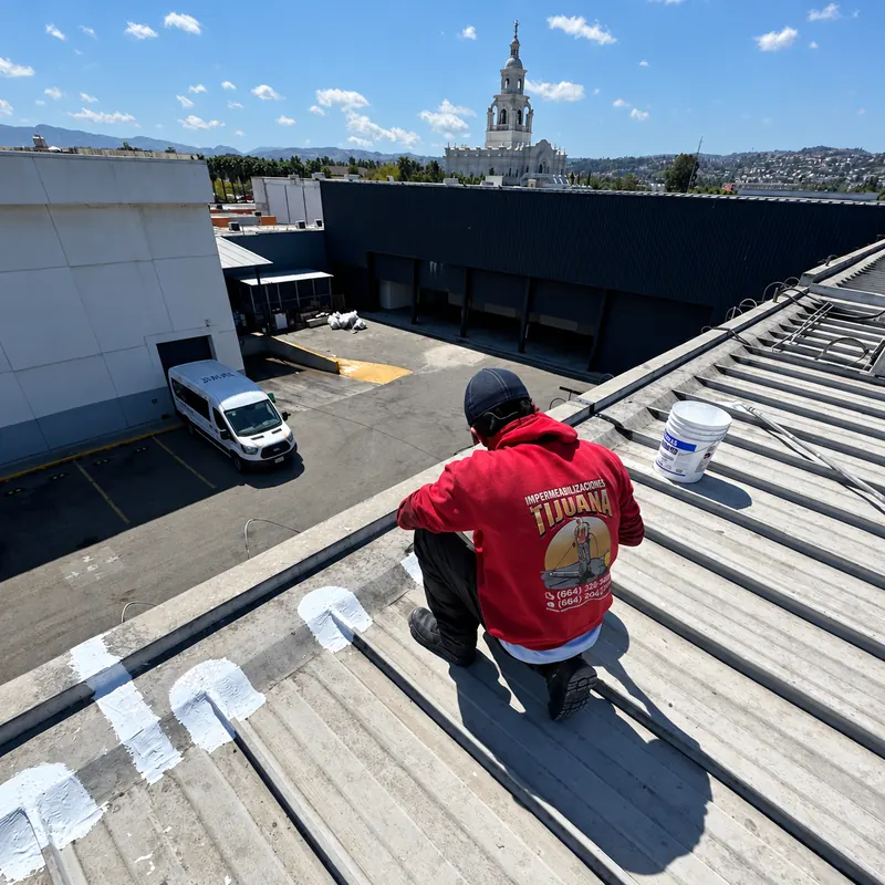 Trabajador arrodillado junto a parches blancos en las juntas de un techo metálico