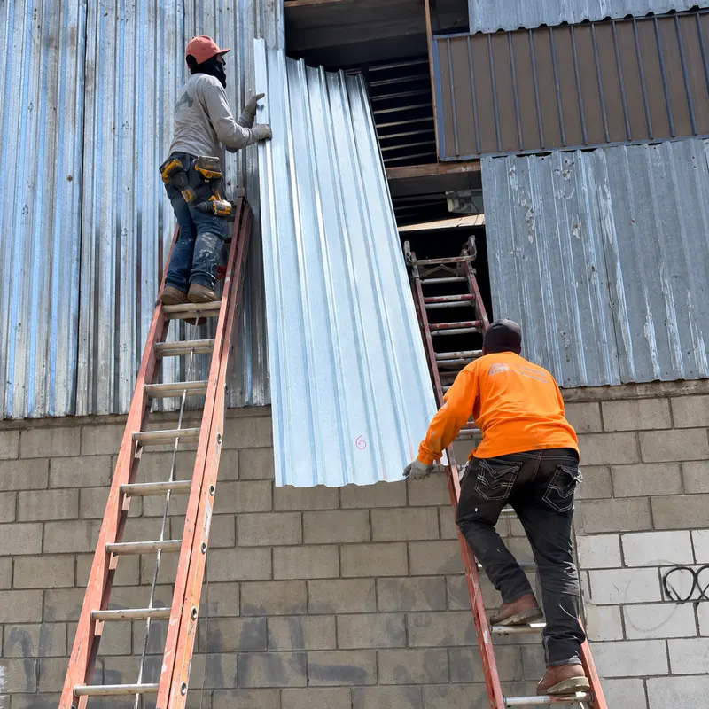 Dos trabajadores en escaleras colocan una lámina acanalada en una fachada