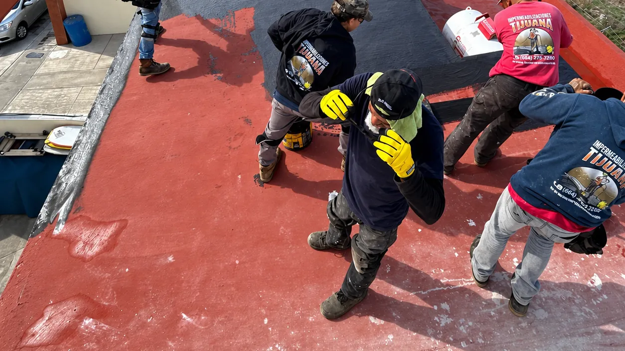 Cuadrilla de cinco trabajadores aplicando recubrimiento sobre una azotea roja