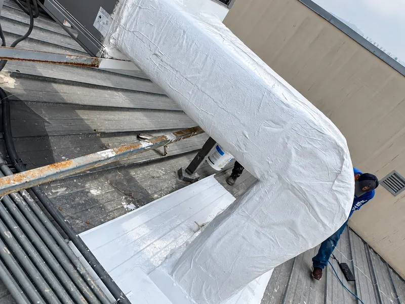 Ducto curvo recubierto conectado a un equipo de climatización, con base sellada en blanco sobre techo metálico