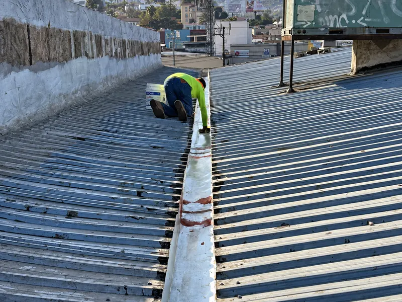 Trabajador arrodillado sella el canalón central entre dos cubiertas de lámina acanalada