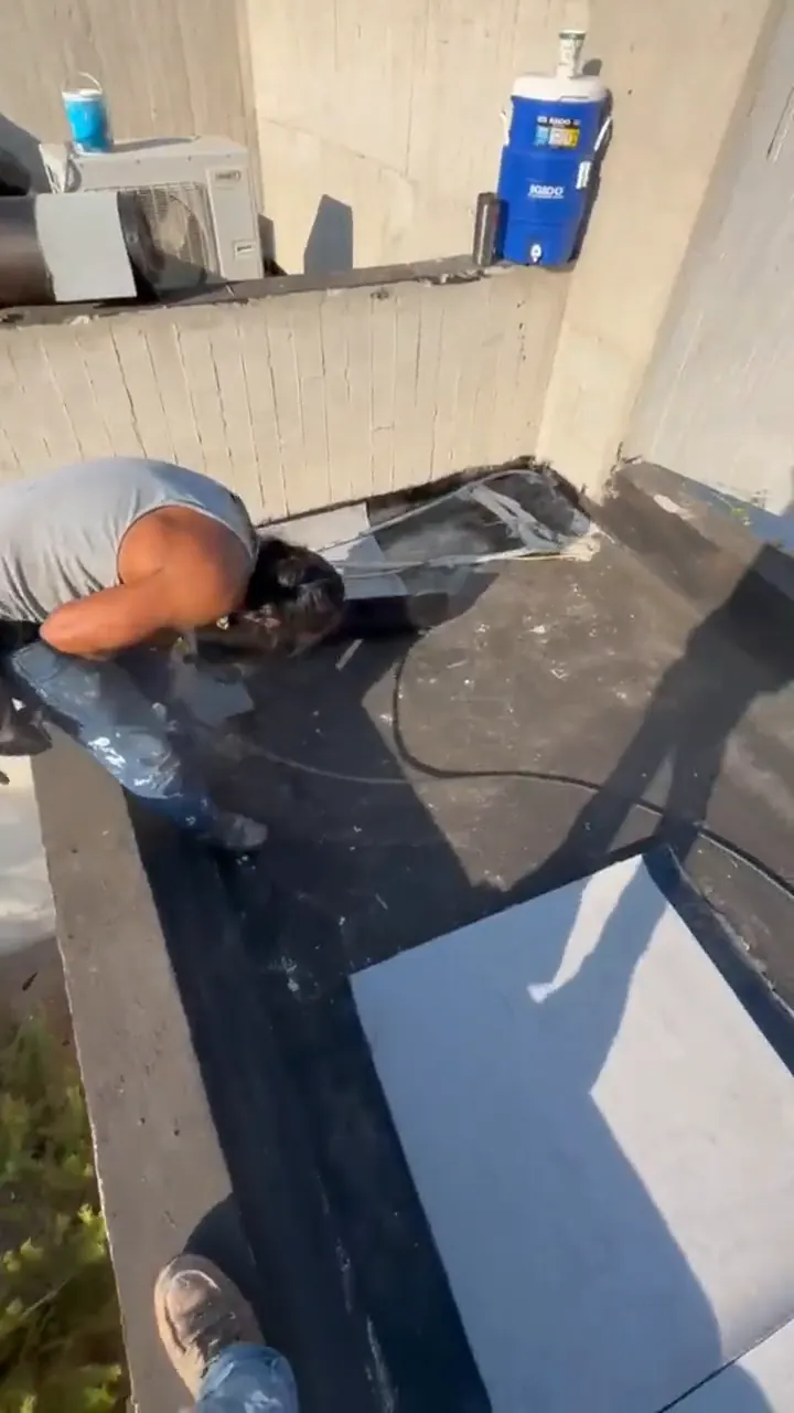 Vista vertical de un trabajador preparando una azotea junto a material de impermeabilización.